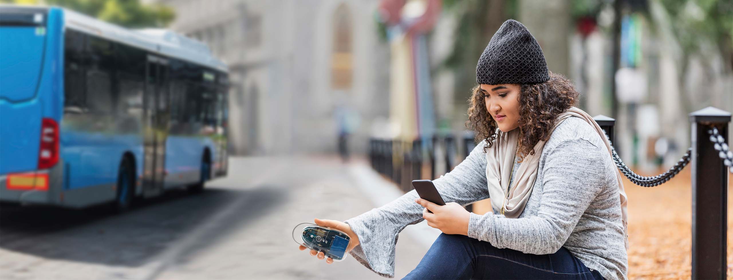 Photo of a female student crouching on a city sidewalk taking measurements with her air quality sensor.