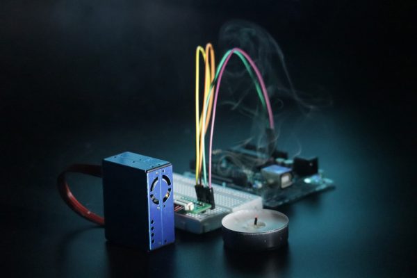 Dramatic photo of an assembled Sensor Build Kit, spotlighted on a black background, with a smouldering candle emitting a smoke plume.