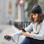 Photo of a female student crouching on a city sidewalk taking measurements with her air quality sensor.