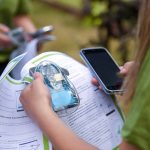 Photo of a student holding an AQ go sensor, a phone, and the Kids Making Sense curriculum