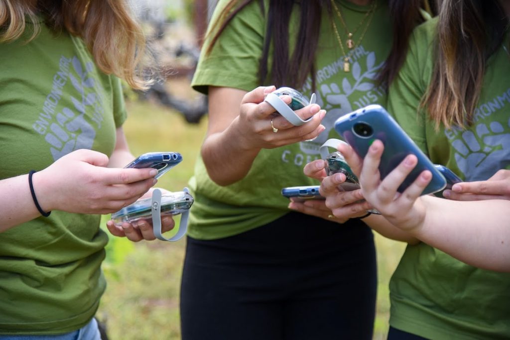 Close up photo of AQ-go sensors and phones held by the hands of four students.