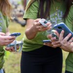 Close up photo of AQ-go sensors and phones held by the hands of four students.